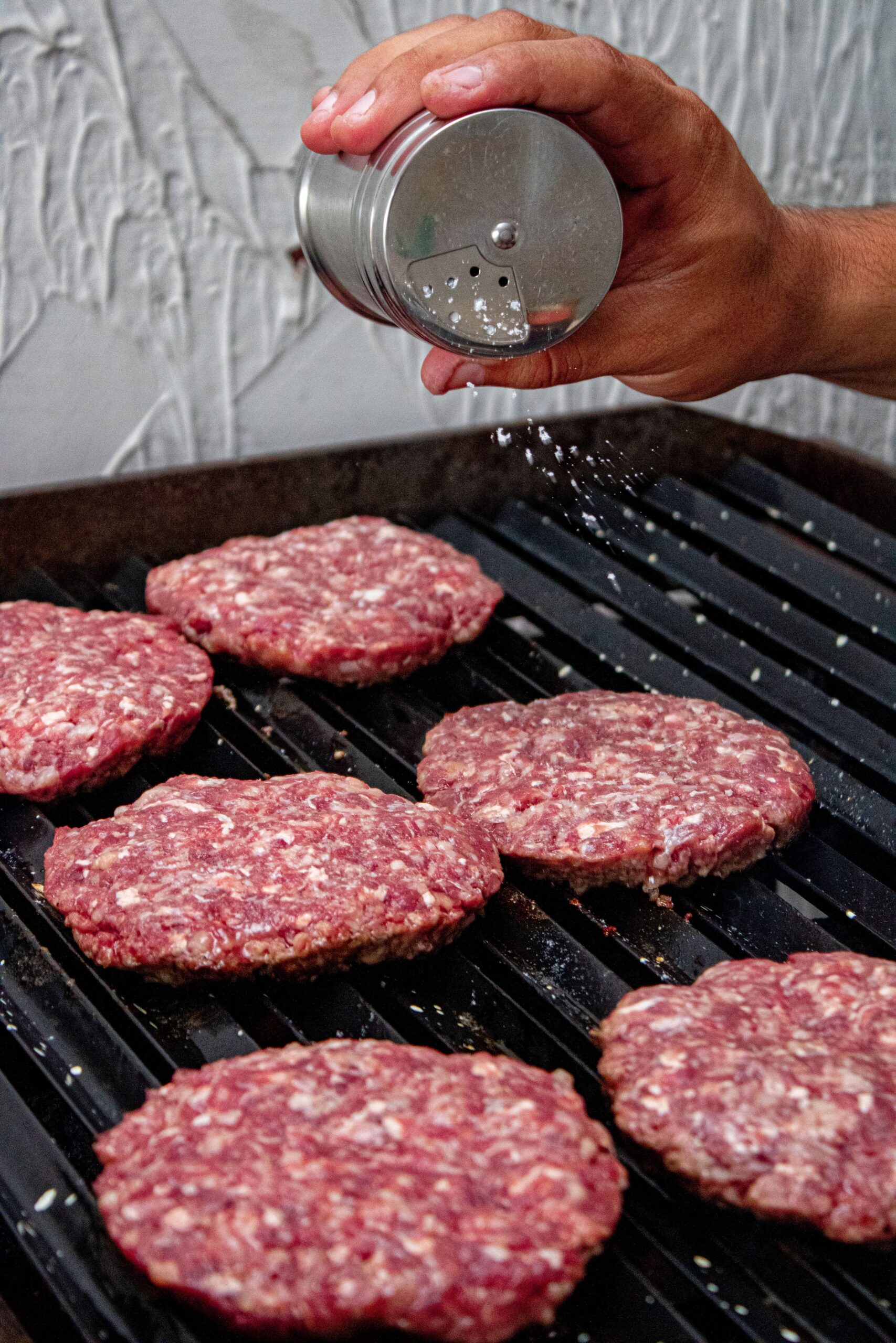 Raw ground meat in a stainless steel bowl, surrounded by fresh herbs, garlic, and pink peppercorns on a rustic wooden board. Ideal for recipes requiring minced meat.